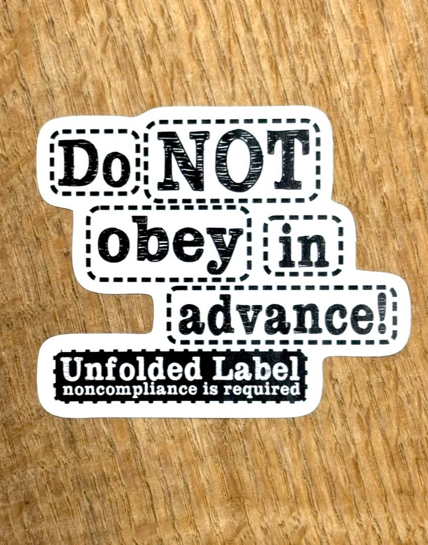 Protest sticker with text 'Do NOT obey in advance! Noncompliance is required' on a wooden surface by Unfolded Label 