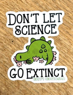 Protests sticker with a green dinosaur and text 'Don't let science go extinct' on a wooden surface by Unfolded Label