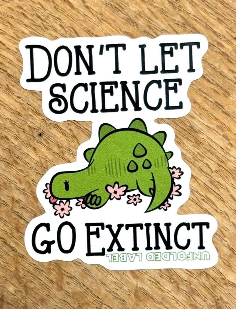 Protests sticker with a green dinosaur and text 'Don't let science go extinct' on a wooden surface by Unfolded Label